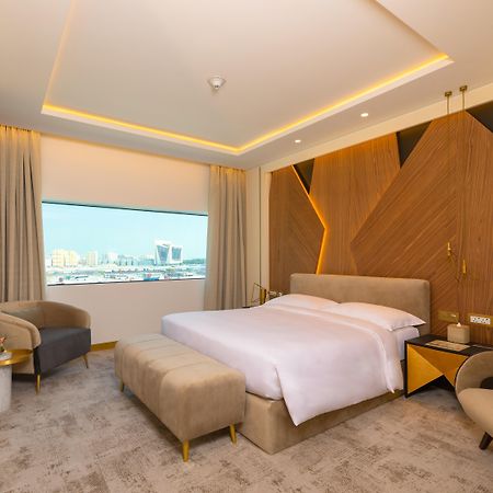 Steigenberger Hotel Ad Dawhah Esterno foto The photo showcases a modern hotel room with a stylish and contemporary design. It features a spacious layout with a large bed placed in the center, dressed in white linens. Behind the bed is an accent wall made of wood, which adds warmth and texture