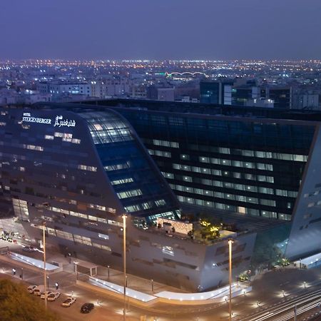 Steigenberger Hotel Ad Dawhah Esterno foto The image shows a modern architectural building, likely a hotel or office structure, illuminated at night. The design features a unique angular shape with large glass windows, reflecting the surrounding city lights. The building appears to be part of
