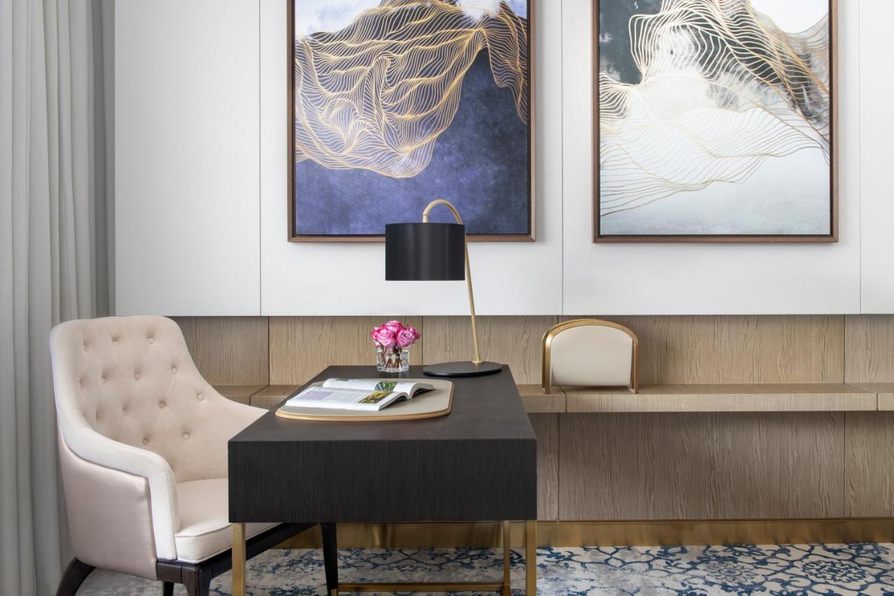 Steigenberger Hotel Ad Dawhah Esterno foto The photo depicts a stylish office or study area. In the foreground, there is a dark wooden desk with a few items on it, including a notepad and a small vase of flowers. A modern black lamp is placed on the desk, providing a sophisticated touch. 

Ad
