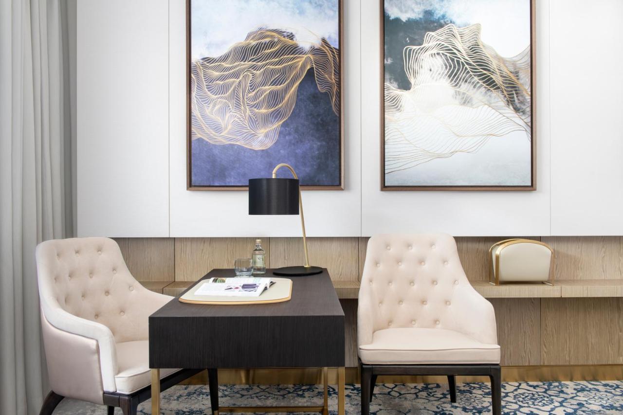 Steigenberger Hotel Ad Dawhah Esterno foto The photo shows a stylish and modern office space. There are two elegant framed artworks on the walls, characterized by abstract designs with soft colors and fluid lines. In the center, there’s a black desk with a white notepad and a pen. A sleek, bl