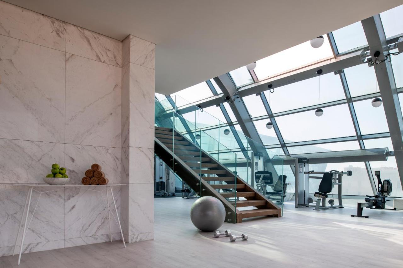 Steigenberger Hotel Ad Dawhah Esterno foto The photo showcases a modern, stylish interior space, likely a gym or fitness area. Key features include:

- **Large Windows**: The room is filled with natural light due to its expansive glass walls and ceiling.
- **Staircase**: A wooden staircase le