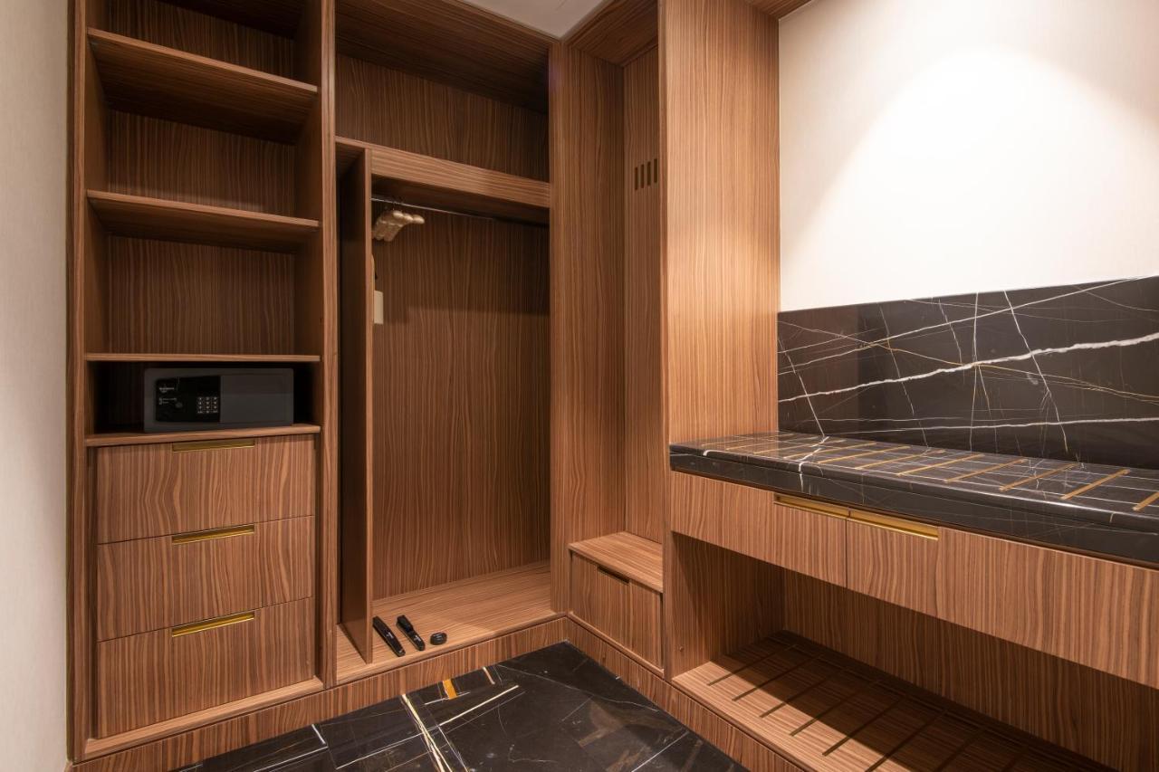 Steigenberger Hotel Ad Dawhah Esterno foto The photo shows a stylishly designed closet or wardrobe area. It features wooden panels with a warm finish. On the left side, there are open shelves, as well as a section for hanging clothes. Below, there are two drawers, adding extra storage space. 
