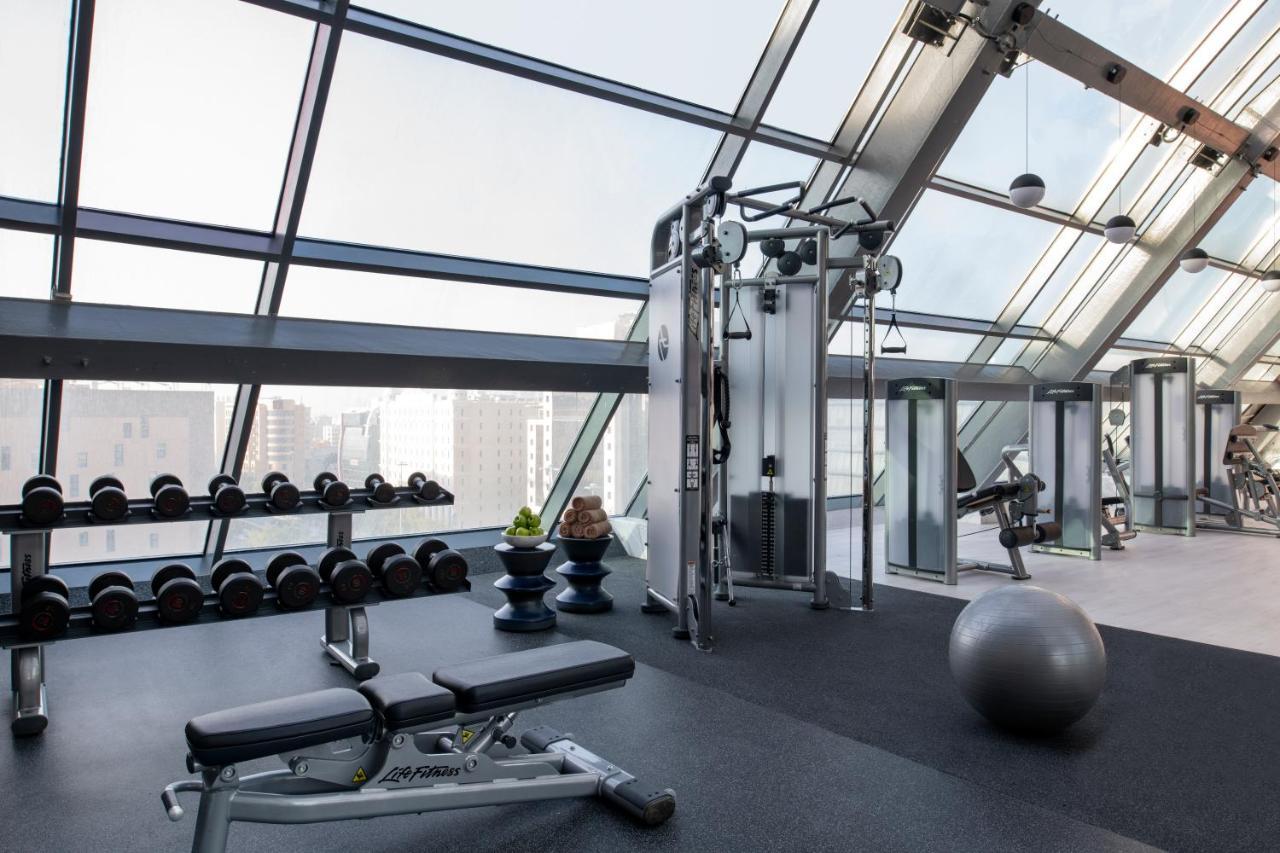 Steigenberger Hotel Ad Dawhah Esterno foto The photo shows a modern gym with large glass windows allowing natural light to fill the space. The gym is equipped with various fitness equipment, including a cable machine, a weight bench, and free weights arranged neatly on a rack. A stability bal