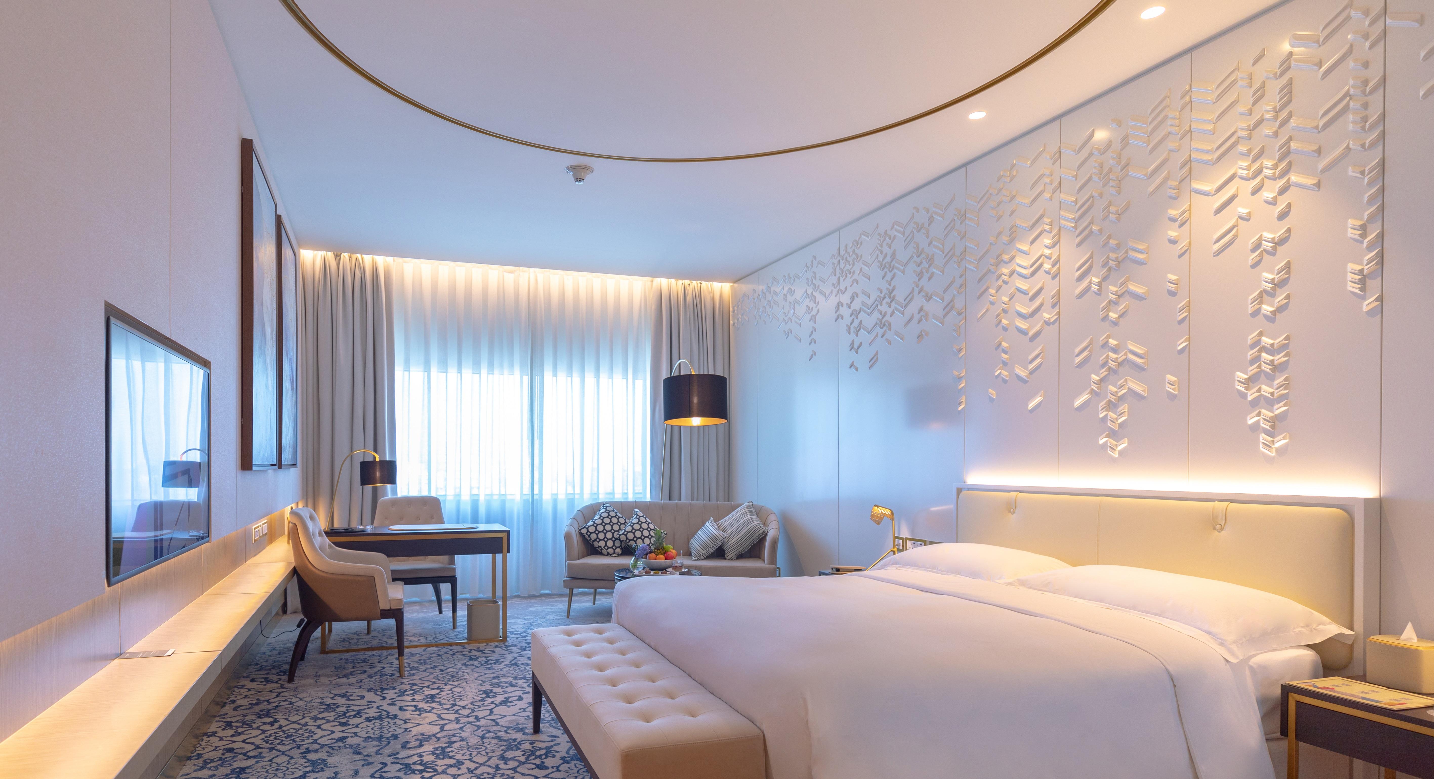 Steigenberger Hotel Ad Dawhah Esterno foto The photo shows a modern and elegantly designed hotel room. It features a large bed with a light-colored headboard and plush bedding. The room includes a seating area with a sofa and armchair, complemented by decorative cushions. There is also a desk