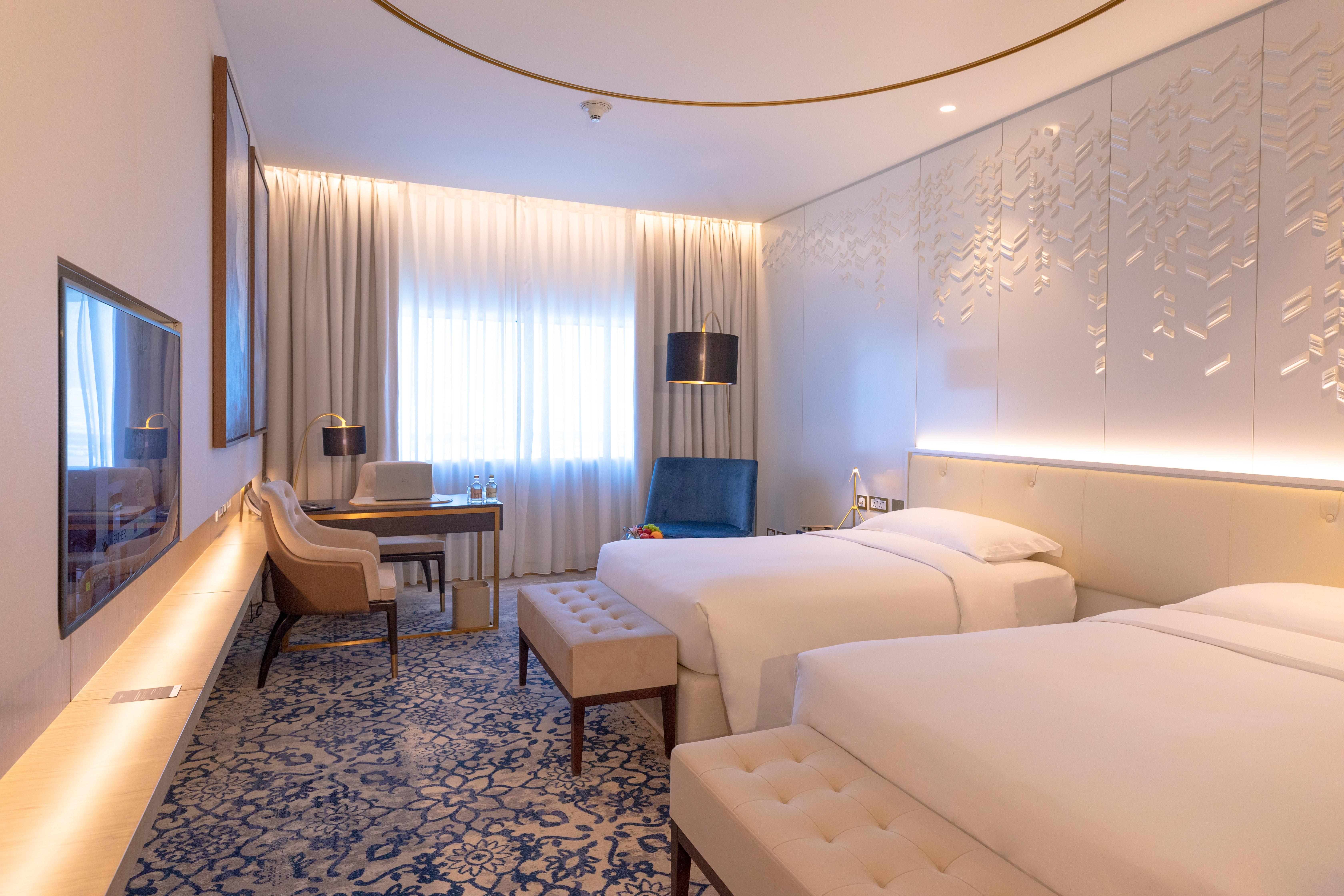 Steigenberger Hotel Ad Dawhah Esterno foto The photo shows a modern hotel room with two single beds placed beside each other. The room features a contemporary design with light-colored walls and stylish decor. There is a large window dressed with sheer curtains, allowing natural light to fill