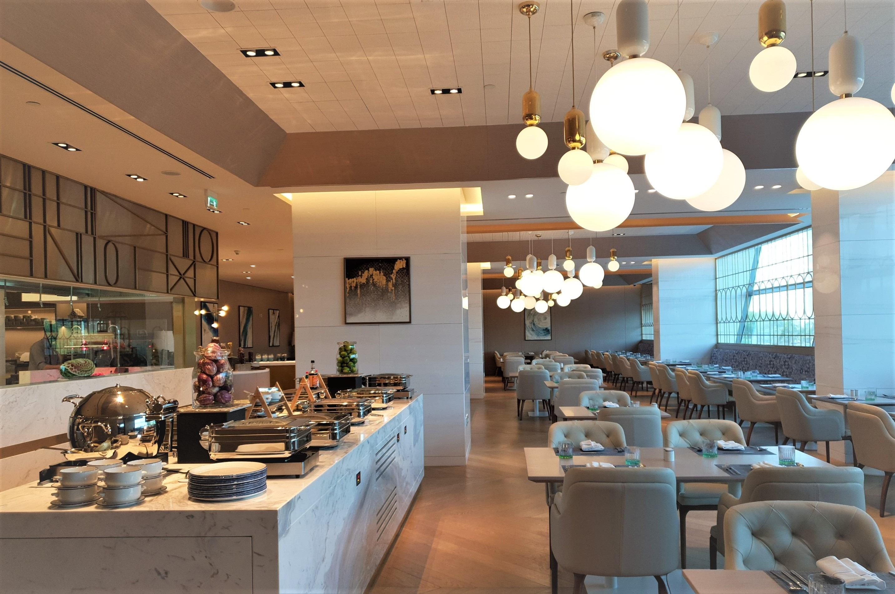 Steigenberger Hotel Ad Dawhah Esterno foto The photo shows the interior of a modern restaurant. It features a well-organized buffet area with various dishes displayed on a marble counter. Elegant dining tables and chairs are set up throughout the space, creating a comfortable atmosphere. The 