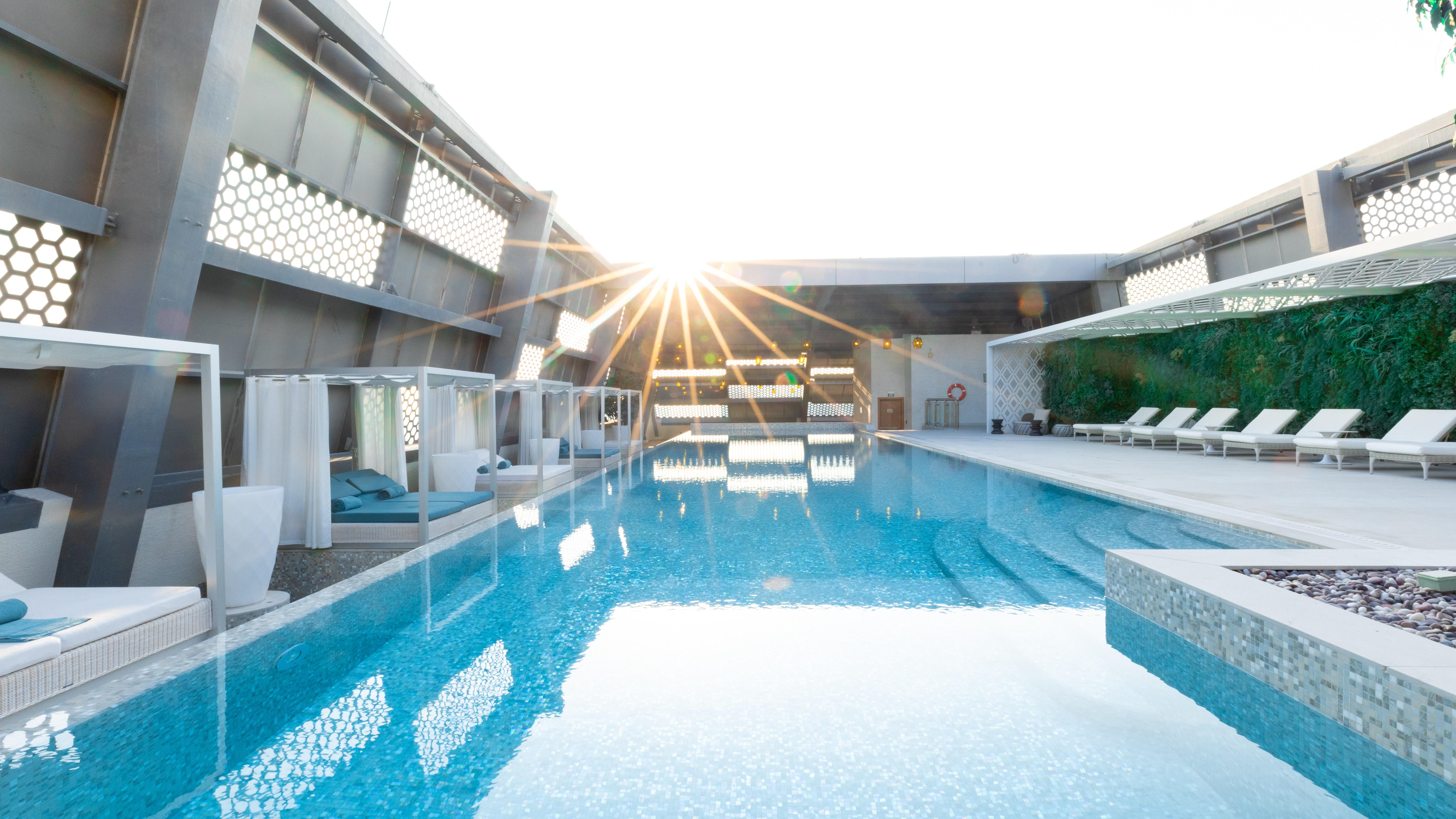Steigenberger Hotel Ad Dawhah Esterno foto The photo shows a modern swimming pool area, likely located on a rooftop, with sunlight shining brightly in the background. The pool features clear, tranquil water that reflects the light and surrounding elements. There are comfortable lounge chairs 