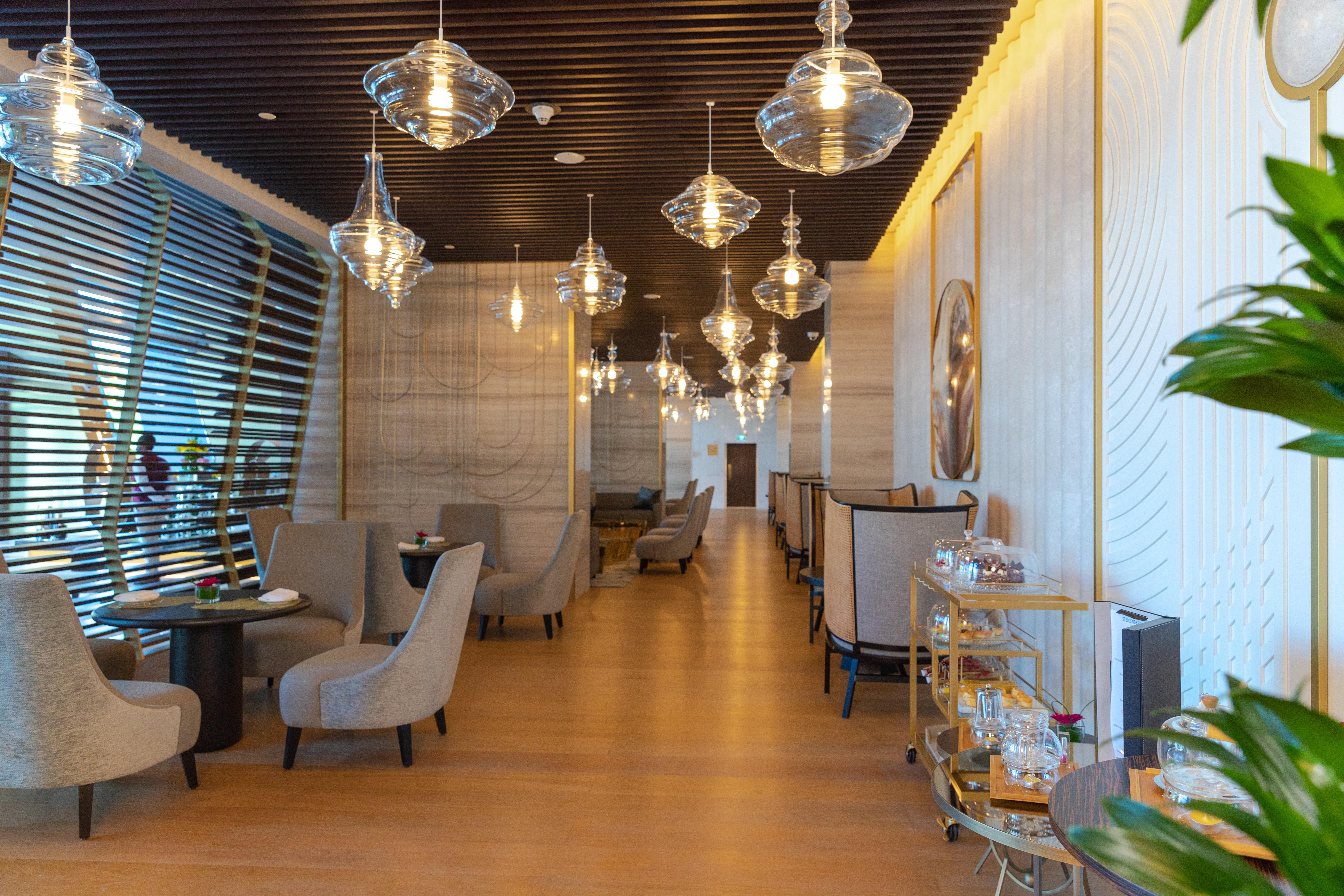 Steigenberger Hotel Ad Dawhah Esterno foto The photo shows the interior of a stylish restaurant. It features modern decor with elegant lighting, including several hanging glass pendant lamps. The seating area consists of plush armchairs arranged around small tables, creating an intimate atmos