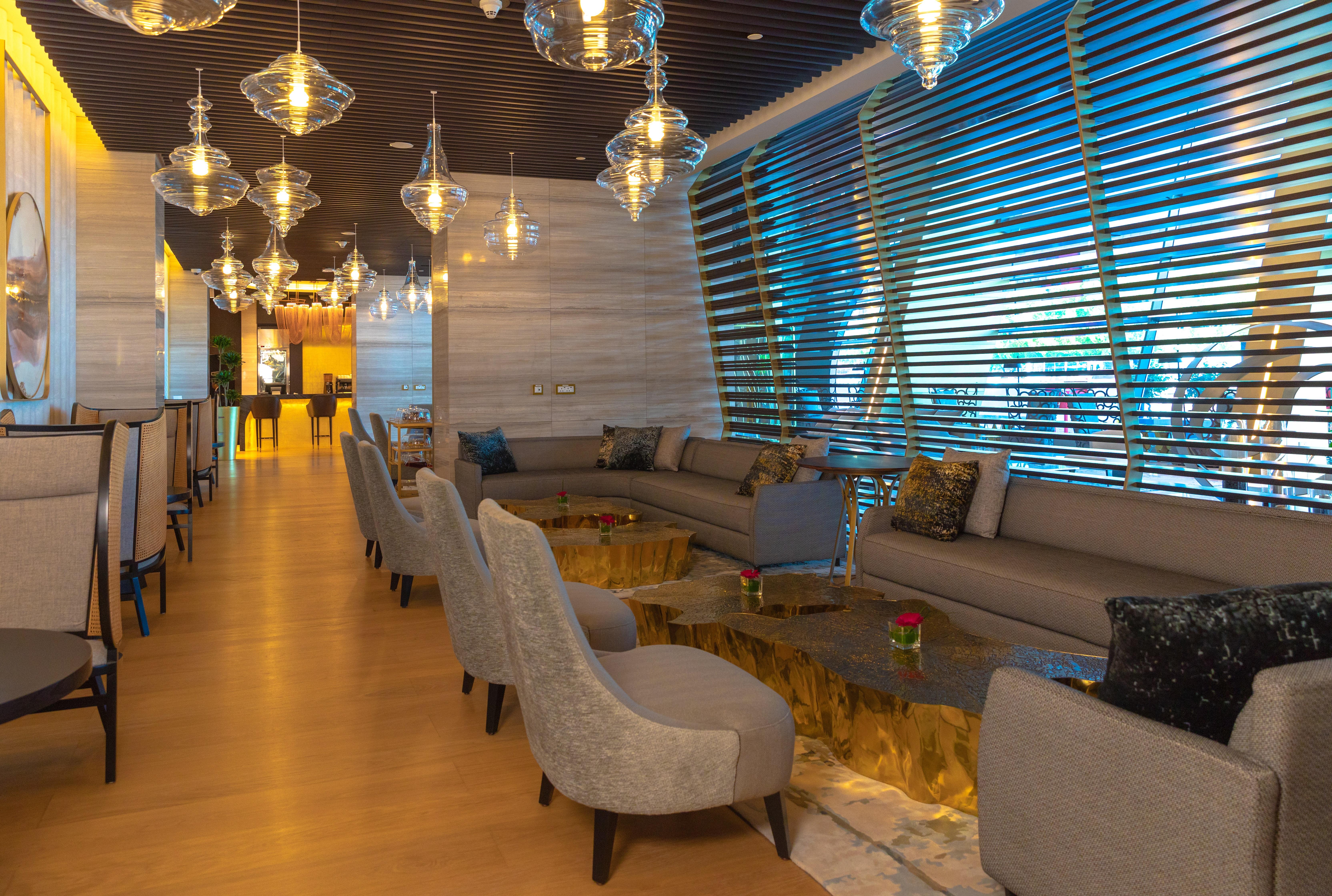 Steigenberger Hotel Ad Dawhah Esterno foto The photo depicts a modern and stylish lounge area. It features a spacious layout with comfortable seating arrangements, including beige sofas and stylish chairs. The tables have a unique design, with a gold-colored base. Ambient lighting is provided