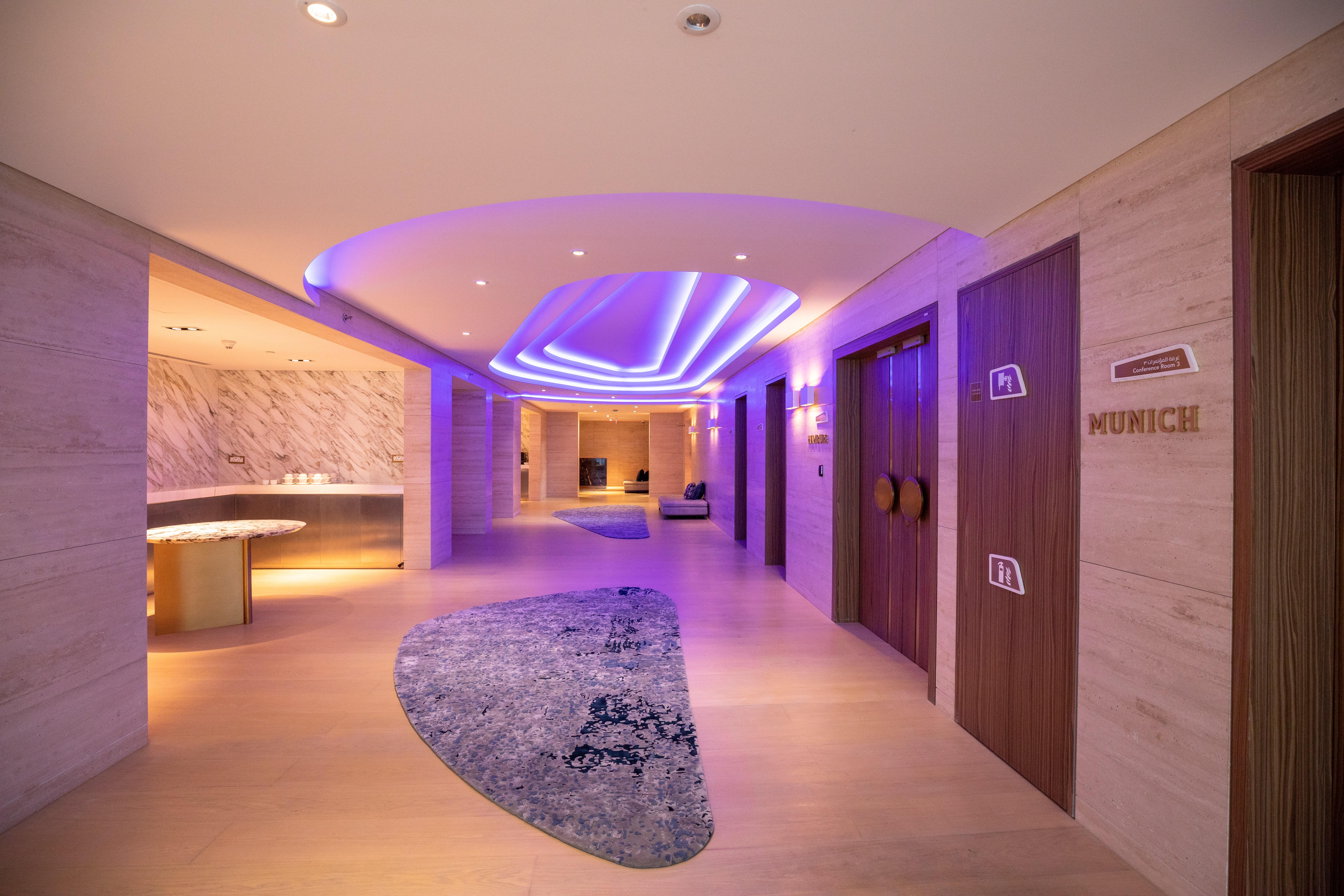 Steigenberger Hotel Ad Dawhah Esterno foto The photo shows a modern hallway in a stylish setting. The corridor features soft, ambient lighting with a purple hue, creating a calming atmosphere. On the left side, there is a curved reception area with a smooth surface. The floor is decorated wit