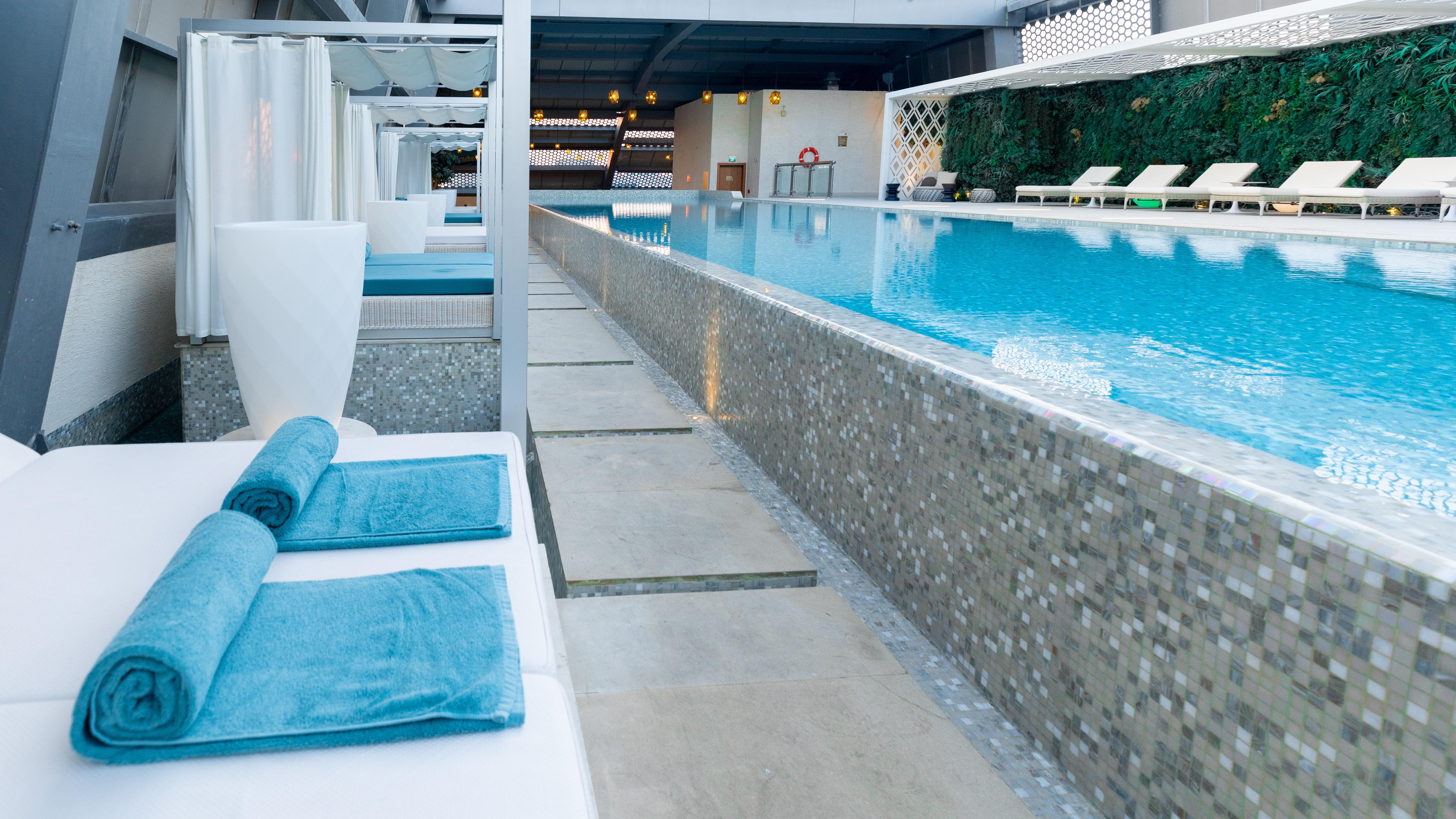 Steigenberger Hotel Ad Dawhah Esterno foto The photo shows a serene swimming pool area featuring a long, rectangular pool with clear blue water. Surrounding the pool are minimalist white lounge chairs and cabanas, creating a relaxing atmosphere. The pool is bordered by a stone or tile pathway