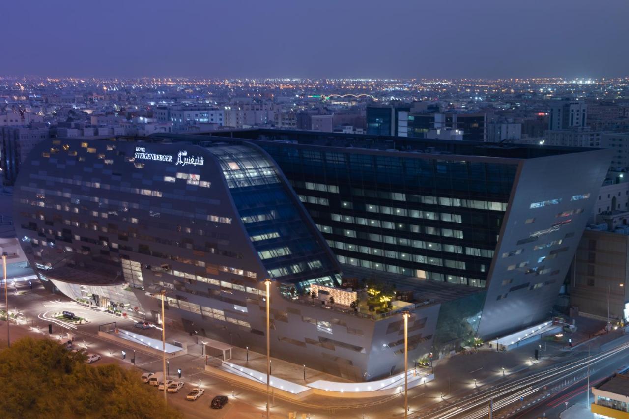Steigenberger Hotel Ad Dawhah Esterno foto The image shows a modern architectural building, likely a hotel or office structure, illuminated at night. The design features a unique angular shape with large glass windows, reflecting the surrounding city lights. The building appears to be part of