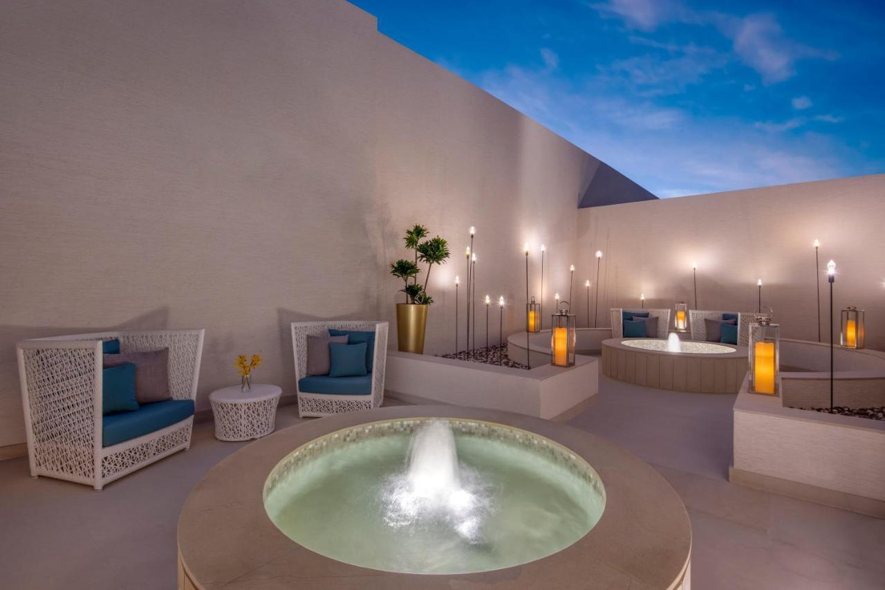 Steigenberger Hotel Ad Dawhah Esterno foto The photo depicts a serene outdoor space featuring a modern and stylish design. Central to the image is a round stone fountain with water gently flowing from it, creating a tranquil atmosphere. Surrounding the fountain are comfortable seating areas w