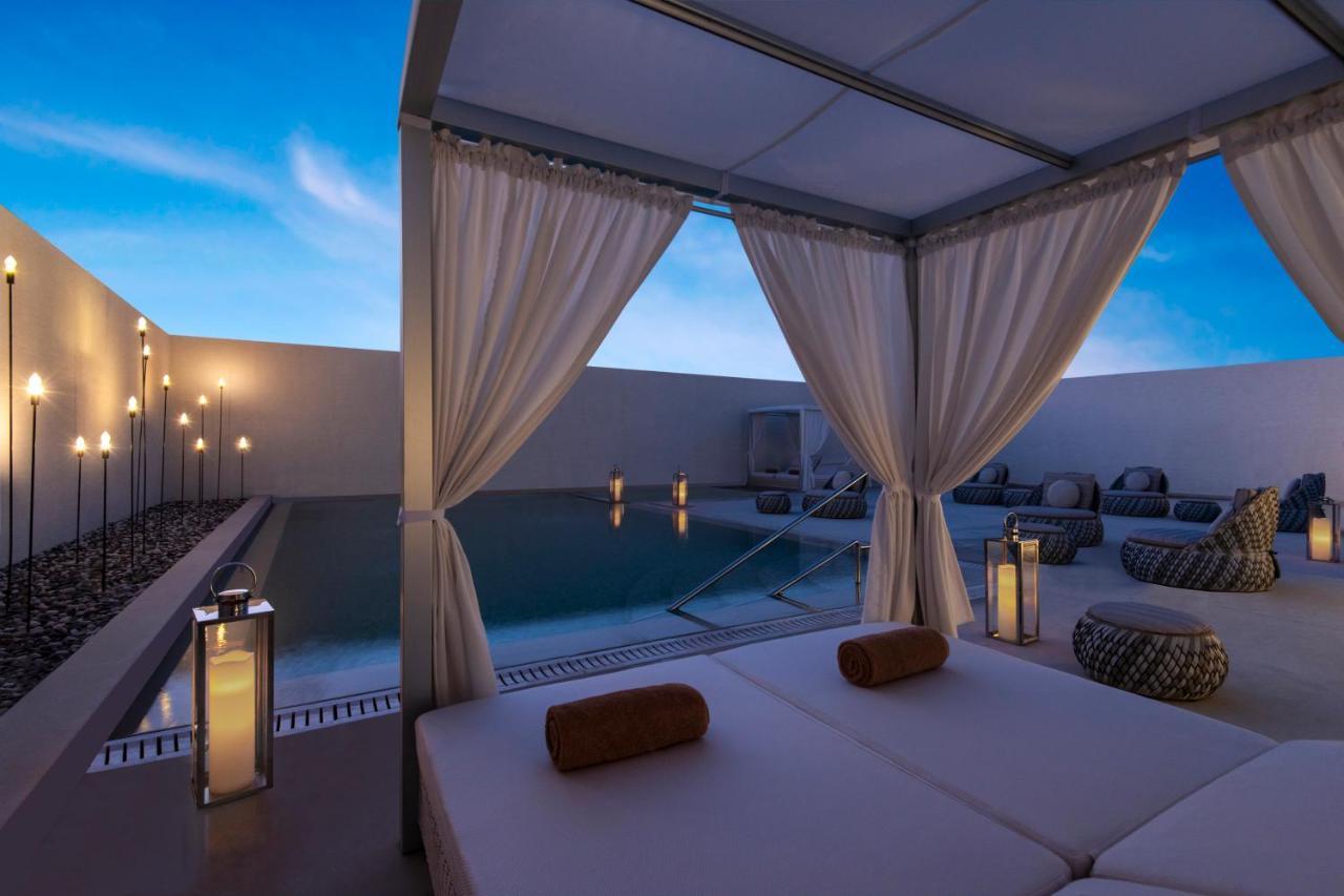 Steigenberger Hotel Ad Dawhah Esterno foto The photo shows a serene outdoor setting, likely at a luxury resort or spa. In the foreground, there is a structure resembling a cabana with sheer white curtains that create a private space. Inside, there are comfortable beds with rolled towels. 

In