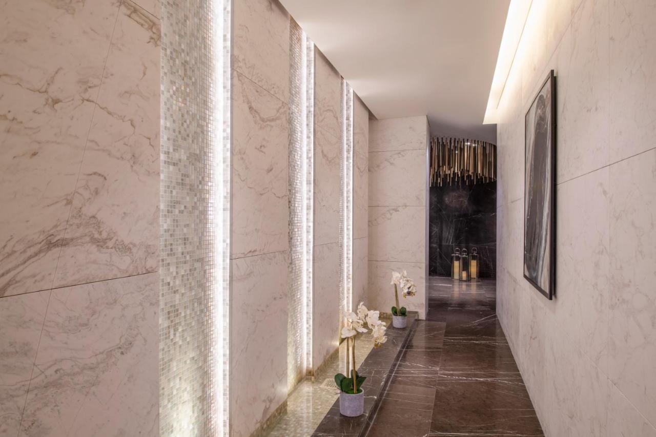 Steigenberger Hotel Ad Dawhah Esterno foto The photo shows a modern hallway with stylish design elements. The walls are made of light-colored marble, and there are vertical strips of lighting integrated into the stone. The floor appears to be a darker stone, providing a contrast to the walls.