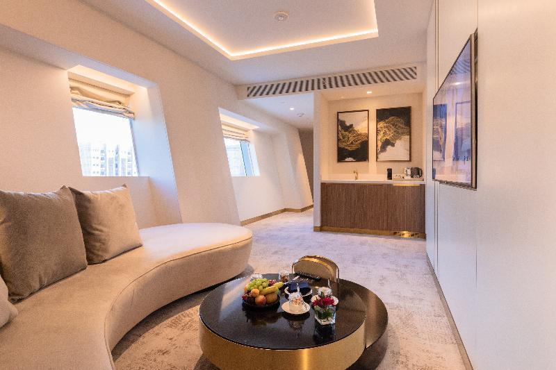Steigenberger Hotel Ad Dawhah Esterno foto The photo shows a modern and stylish interior space, likely a lounge or a living area. It features a curved sofa in a light color, providing a comfortable seating arrangement. In the center, there is a round coffee table adorned with a selection of f