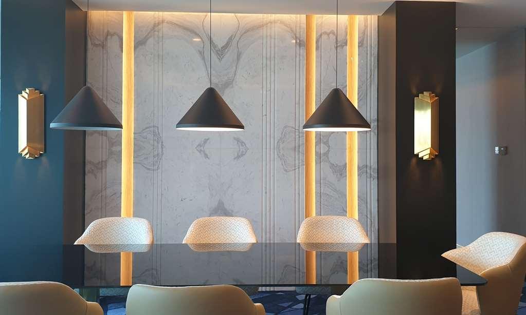 Steigenberger Hotel Ad Dawhah Camera foto The photo showcases a modern interior space featuring a sleek design. The focal point is a wall adorned with a marble-like texture, enhanced by vertical lighting strips that add warmth to the environment. Above a table or counter are three pendant li