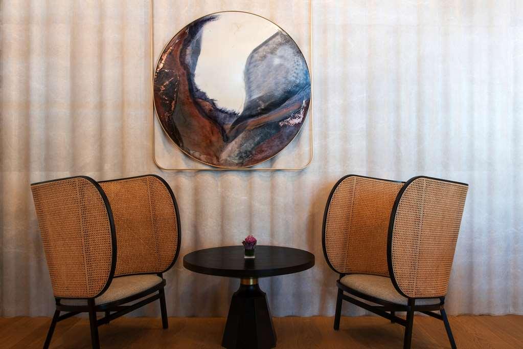 Steigenberger Hotel Ad Dawhah Ristorante foto The photo showcases a stylish and modern seating area featuring two elegantly designed chairs with curved, woven backs and light-colored cushions. Between the chairs is a small round table with a black base. Above the table hangs a large circular art